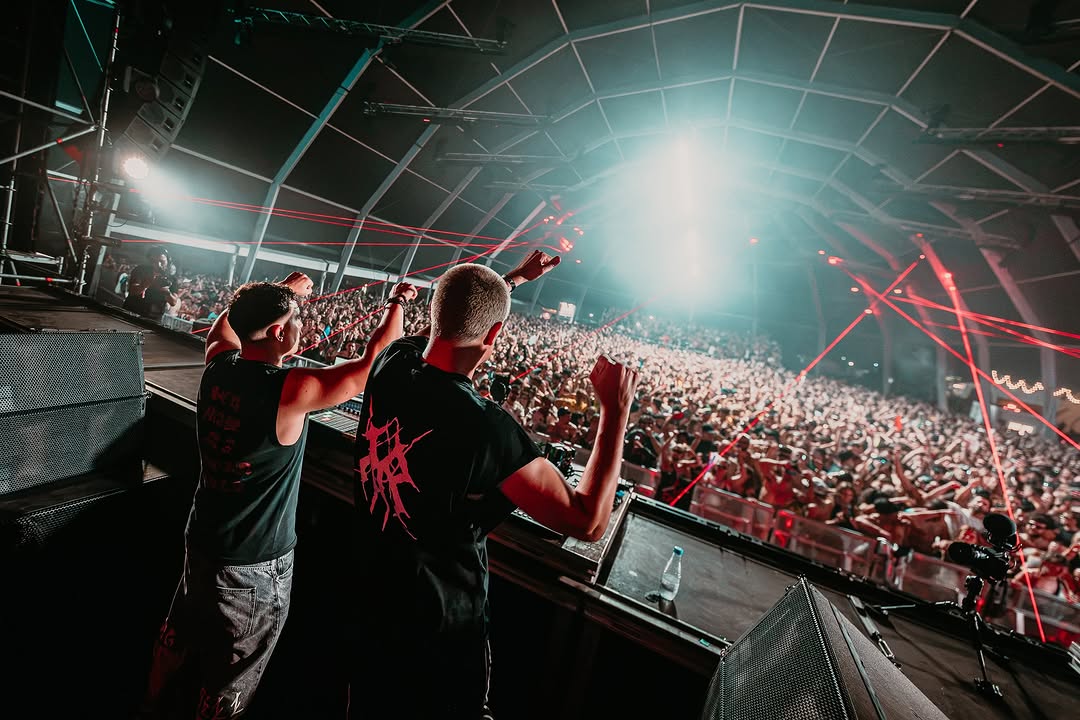 Dos artistas celebrando sobre el escenario con láseres rojos