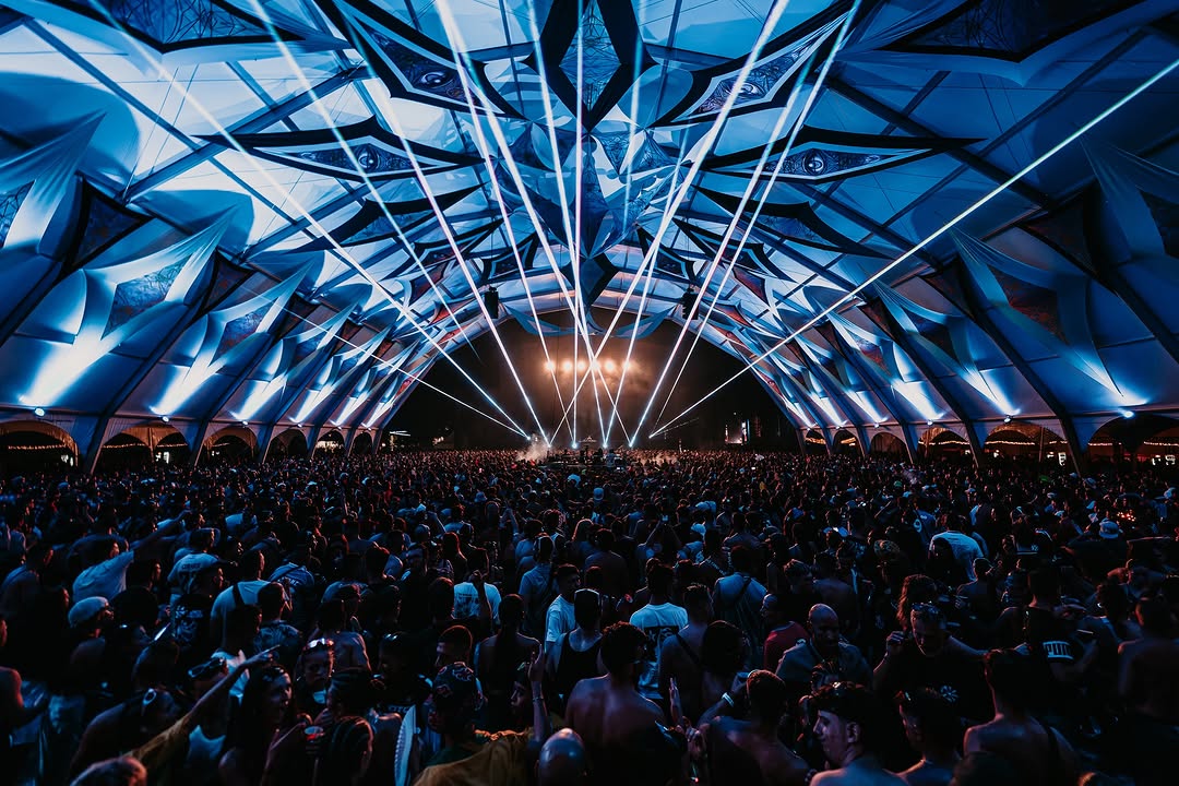 Vista frontal de la carpa azul con haces de luz sobre miles de personas
